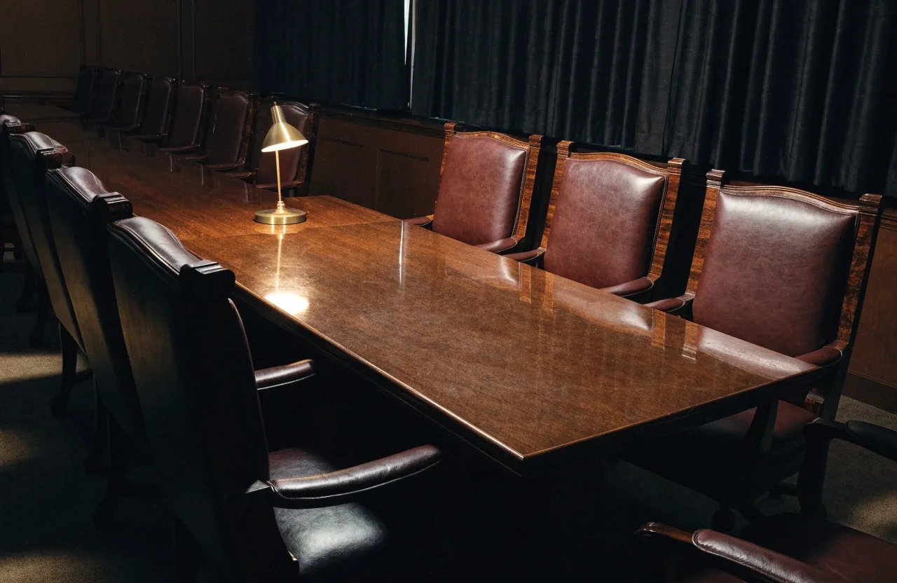 A single sheet of newsprint and a pencil on a warm wooden newsroom table under a low lamp